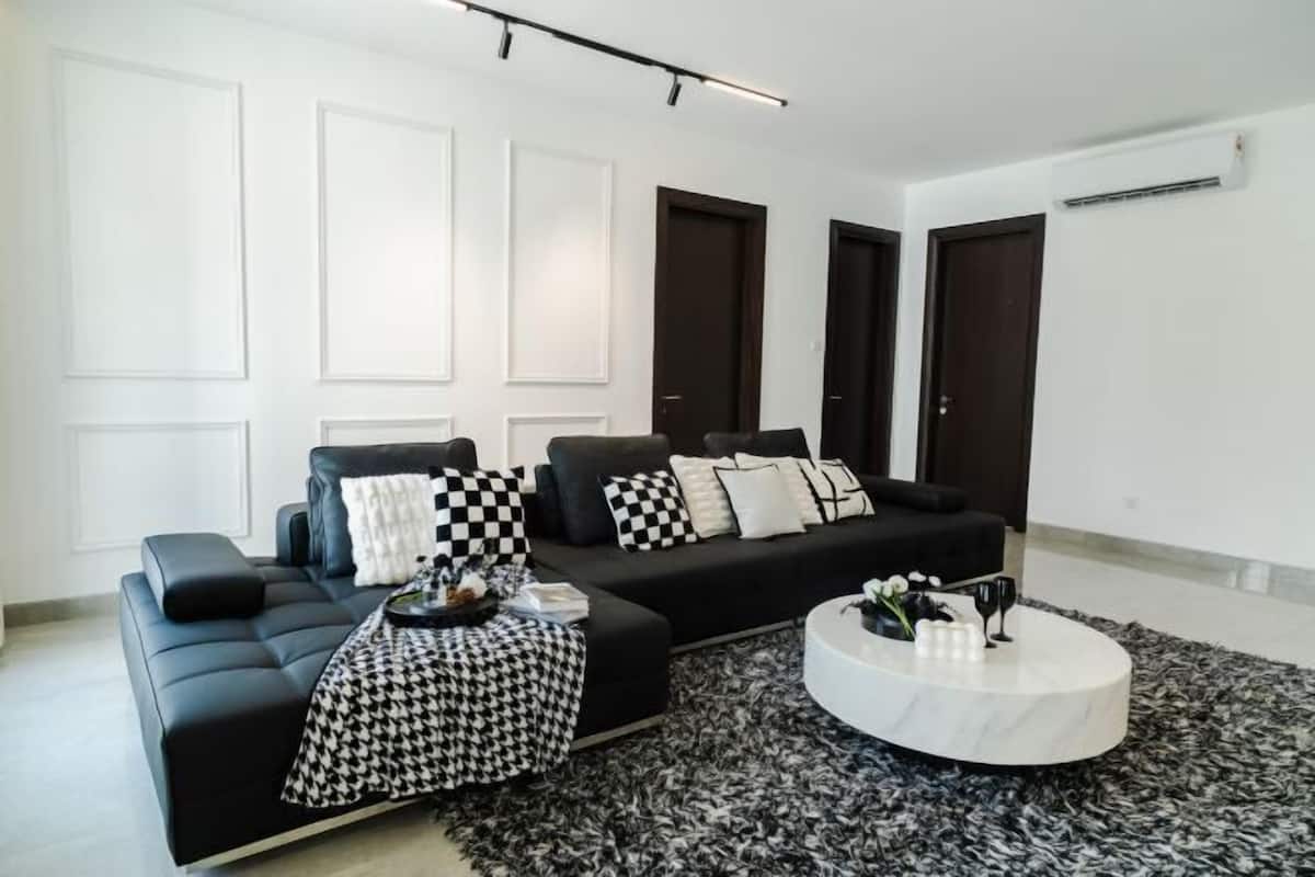 Ein modernes Wohnzimmer mit einem schwarzen Sofa, einem runden Couchtisch und einem gemusterten Teppich.