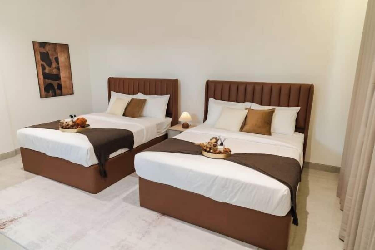 Ein Hotelzimmer mit zwei Betten, jeweils mit brauner Kopfteil, weißer Bettwäsche und einem kleinen Tisch mit Obstschale.