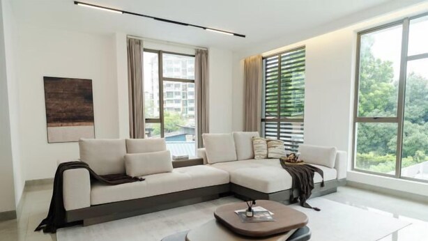 Un salon moderne avec un canapé d’angle, une table basse et de grandes fenêtres donnant sur l’extérieur.