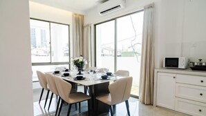 Un espace repas moderne avec une table dressée pour six personnes, une cuisine équipée d’un four à micro-ondes et de grandes fenêtres offrant une vue sur la ville.