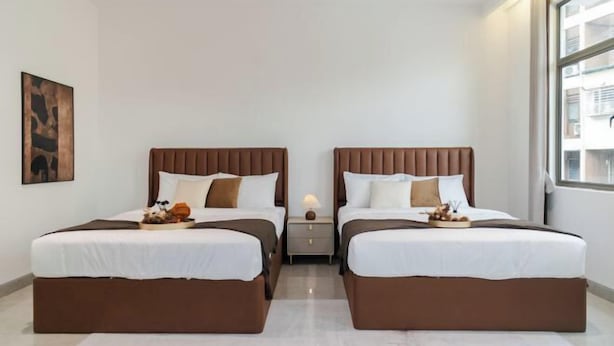 Une chambre d’hôtel avec deux lits, une table de chevet, une lampe et une fenêtre donnant sur un beau paysage.