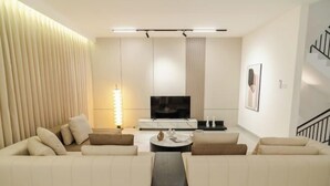 Un salon moderne comprenant un ensemble de canapés, un téléviseur à écran plat, une table basse et un luminaire fixé au mur.