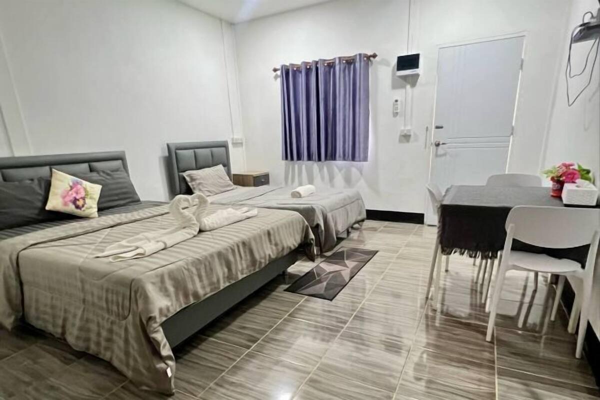 A hotel room with two beds, a dining table with chairs, a window with curtains, and a door.
