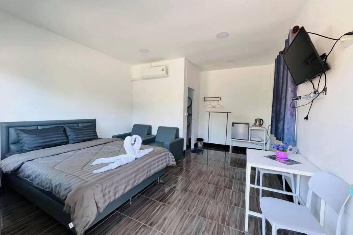 A hotel room with a bed, a desk, a chair, a television mounted on the wall, and a small table with a vase.