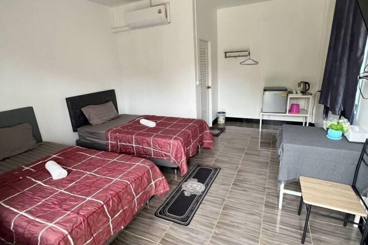 A hotel room with two beds, a small table with a chair, a desk, a hanging coat rack, and a wall-mounted air conditioner.