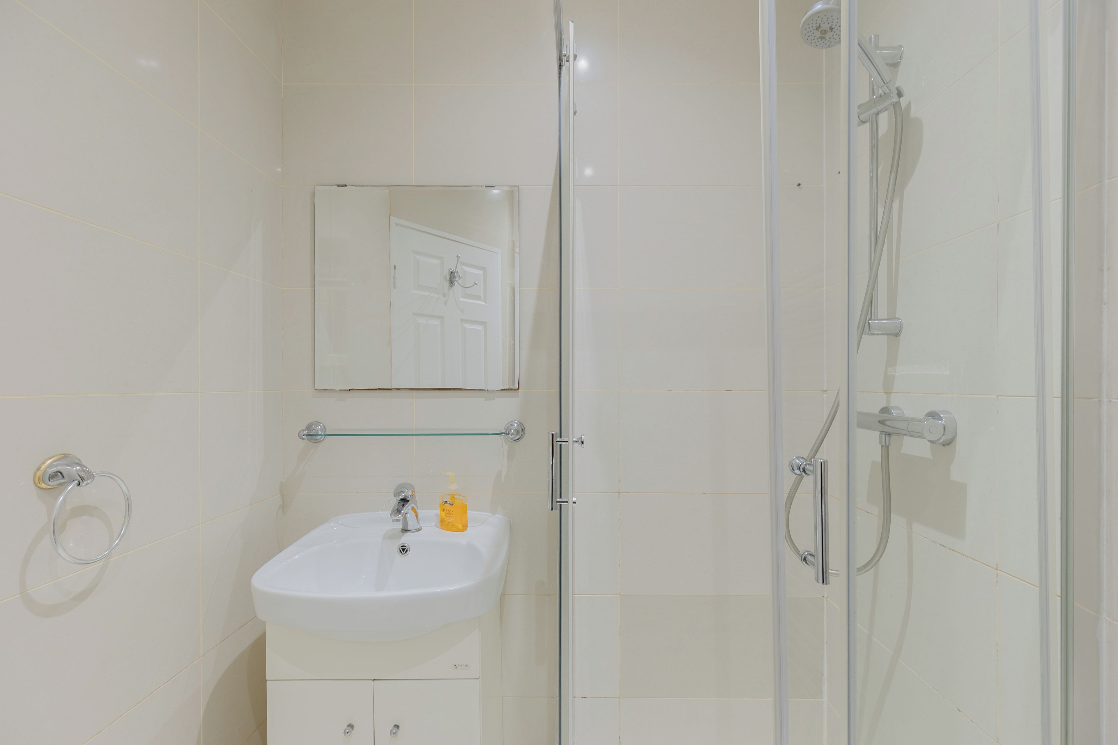 Un baño con un lavamanos blanco, cabina de ducha con mampara de vidrio y un espejo sobre el lavamanos.