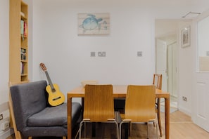 A dining area with a wooden table, two chairs, a guitar, and a bookshelf.