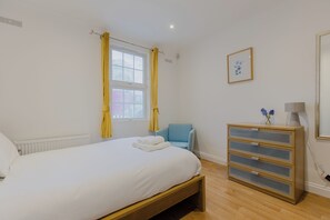 Une chambre à coucher comprenant un lit, une chaise, une table de chevet avec une lampe et un tableau accroché au mur.
