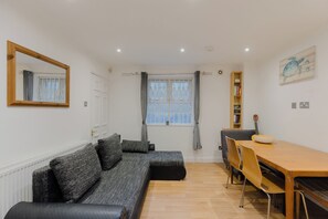 A modern living room with a sofa, a dining table, and a kitchen area.