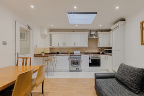 A compact kitchen with white cabinets, a washing machine, and a dining area with a wooden table and chairs.