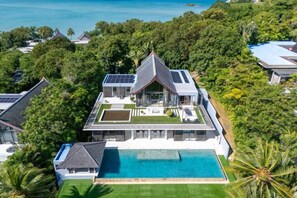 En stor bolig med swimmingpool, omgivet af frodig vegetation og havudsigt.