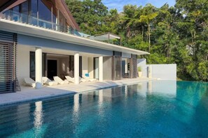 Et moderne hus med swimmingpool, store vinduer og udsigt til træer.