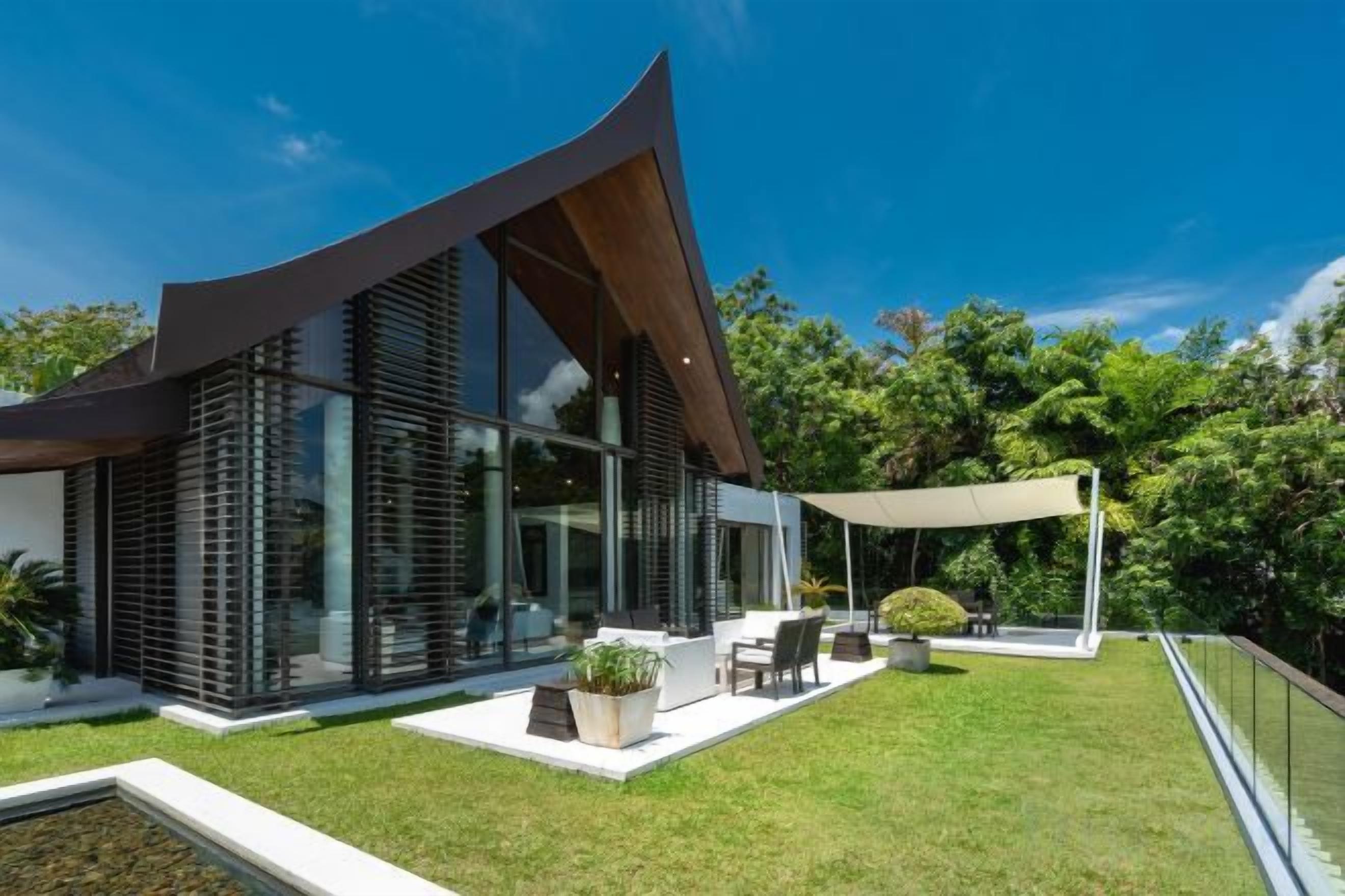 A modern house with a sloped roof, large windows, and a patio area with outdoor furniture.