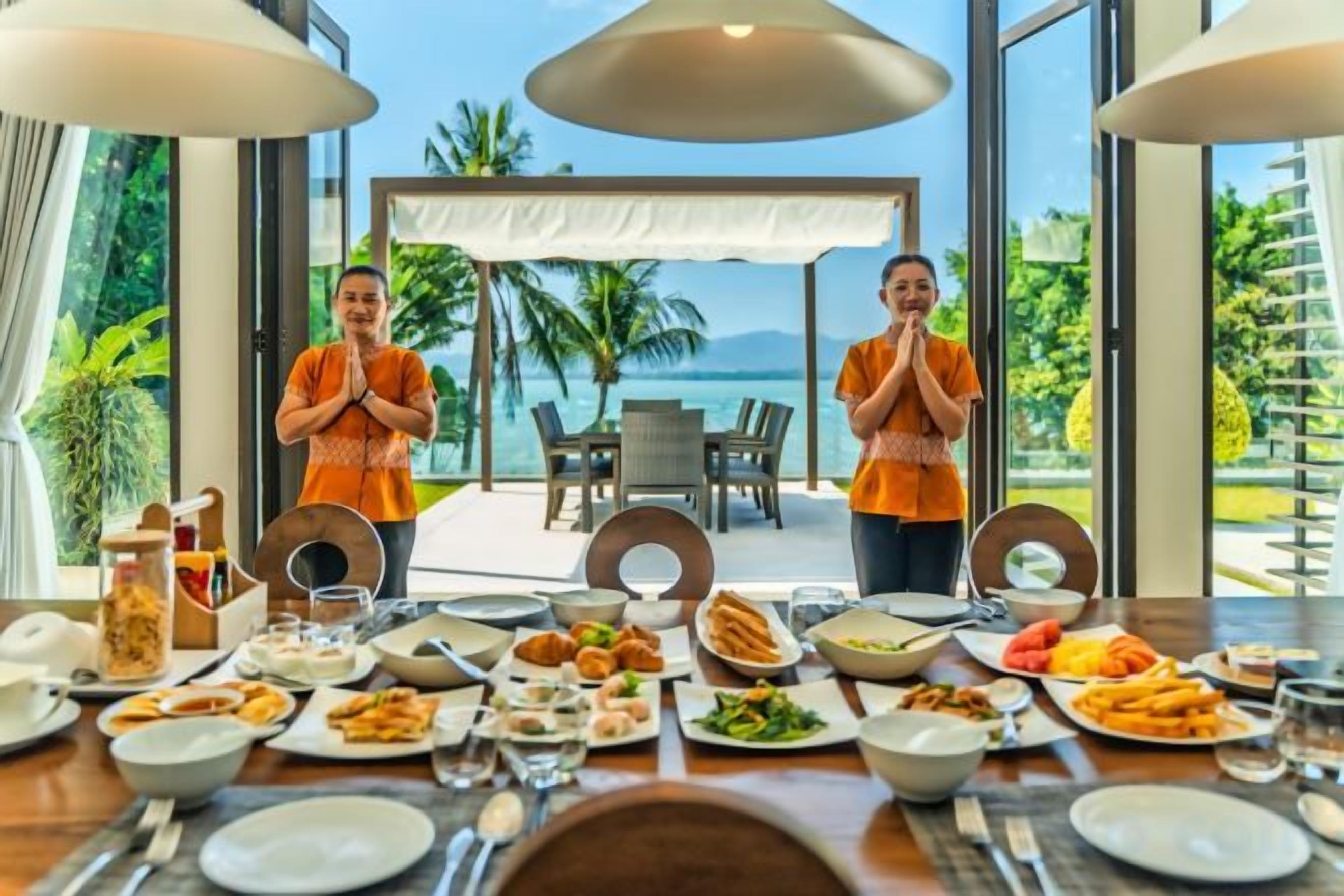 A dining table set for a meal with a view of the ocean and palm trees.