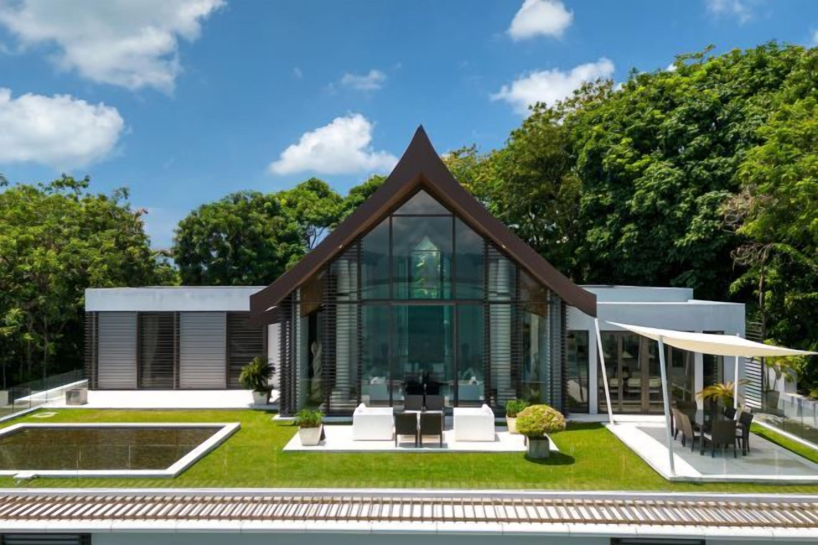 A modern house with a glass facade, a triangular roof, and a patio with outdoor furniture.