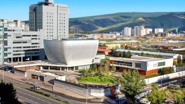 Un edificio moderno con una estructura esférica distintiva, rodeado de otros edificios contemporáneos y un cielo despejado.