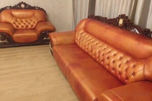 A brown leather sofa with a tufted backrest and armrests, positioned in a room with a wooden floor and a curtain in the background. - OYU (Ulaanbaatar)