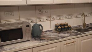 Una cocina con armarios blancos, microondas, hervidor y pileta.