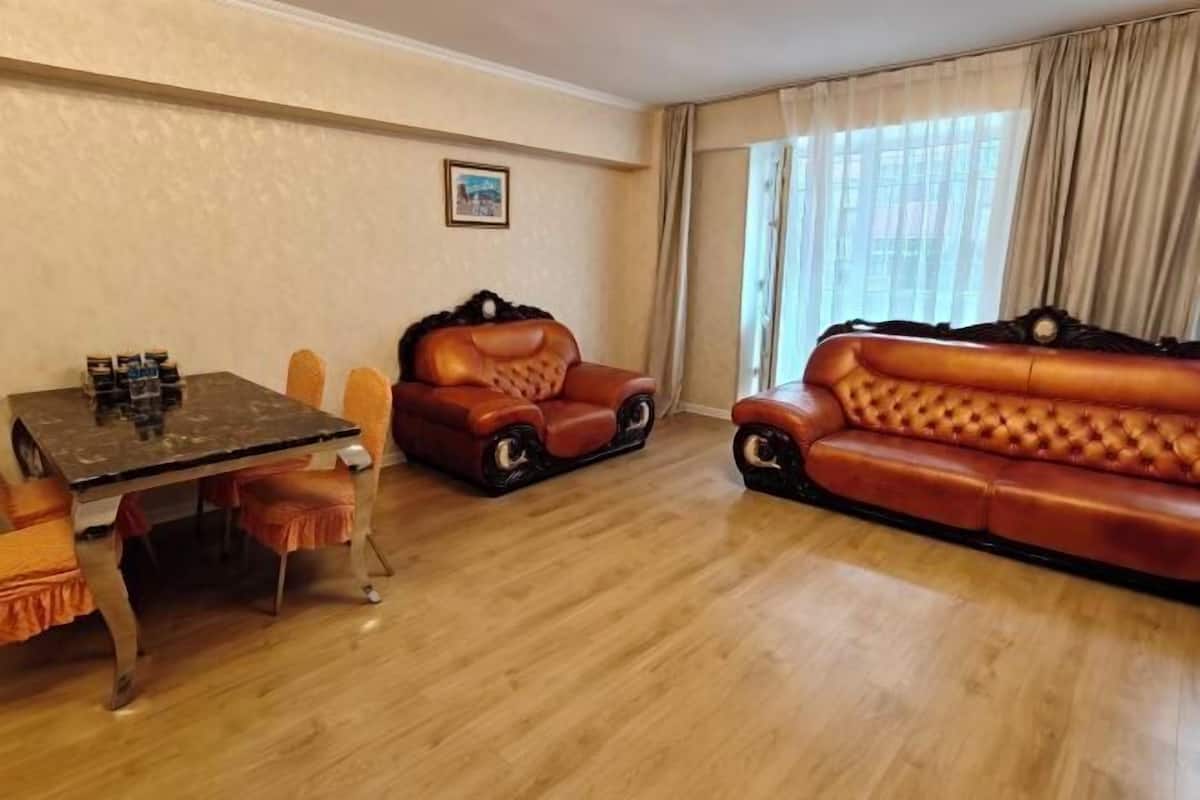 A room with a dining table, two leather sofas, and a window with curtains.