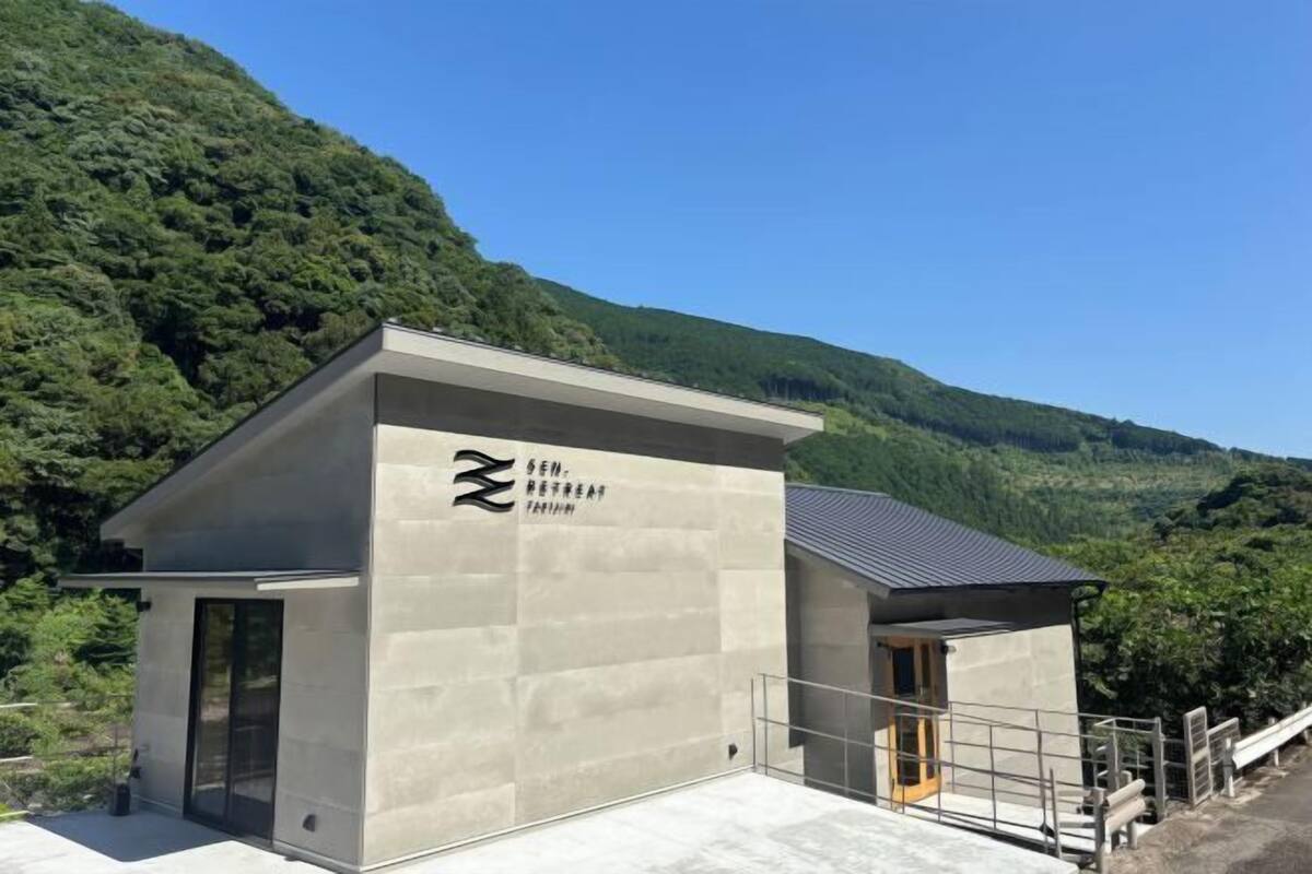 A modern building with a minimalist design, featuring a large logo on the facade, situated in a lush, green mountainous area.