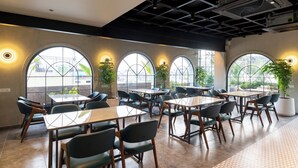 A modern dining area with multiple tables and chairs, large windows with geometric designs, and potted plants. - Champion Prime-My Downtown Hotel (Udaipur)