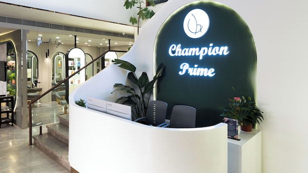 A hotel reception area with a curved reception desk, a large flat-screen TV mounted on the wall, and a staircase leading to an upper floor. - Champion Prime-My Downtown Hotel (Udaipur)