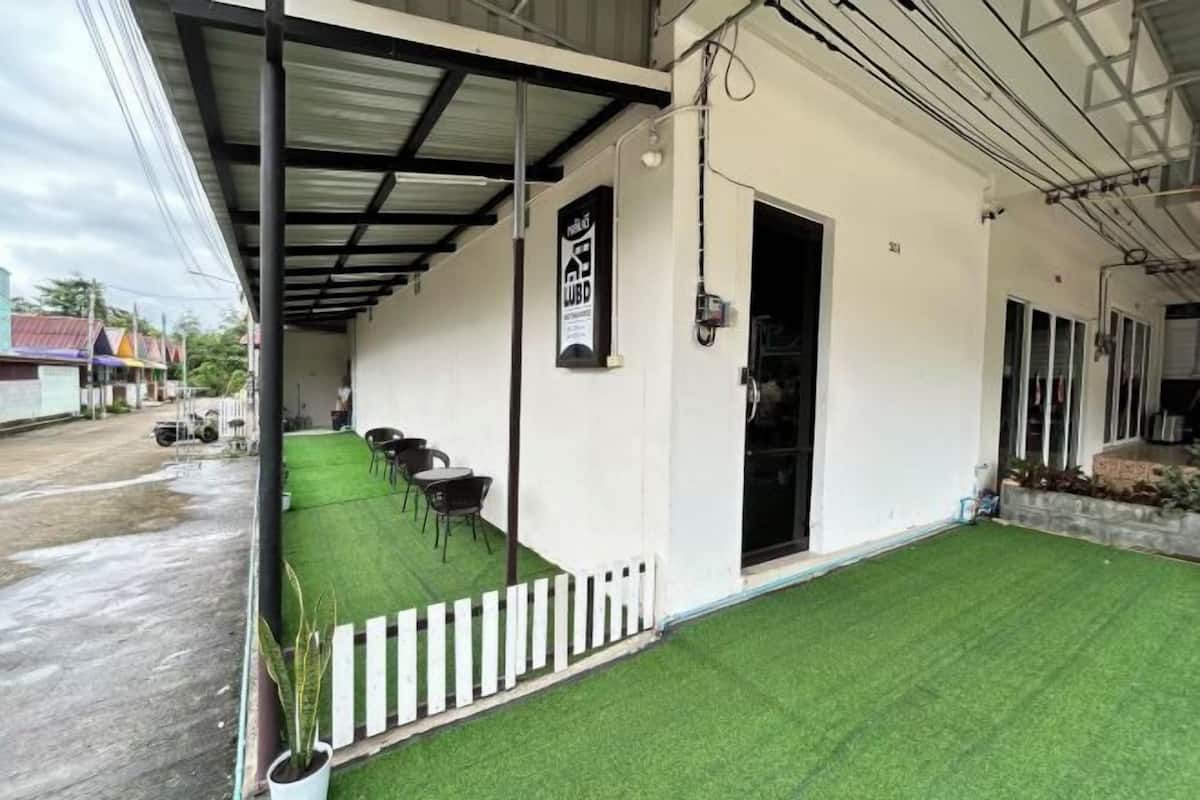 Un espacio al aire libre techado con césped artificial, una cerca de piquetes blancos y una puerta que da a un edificio.