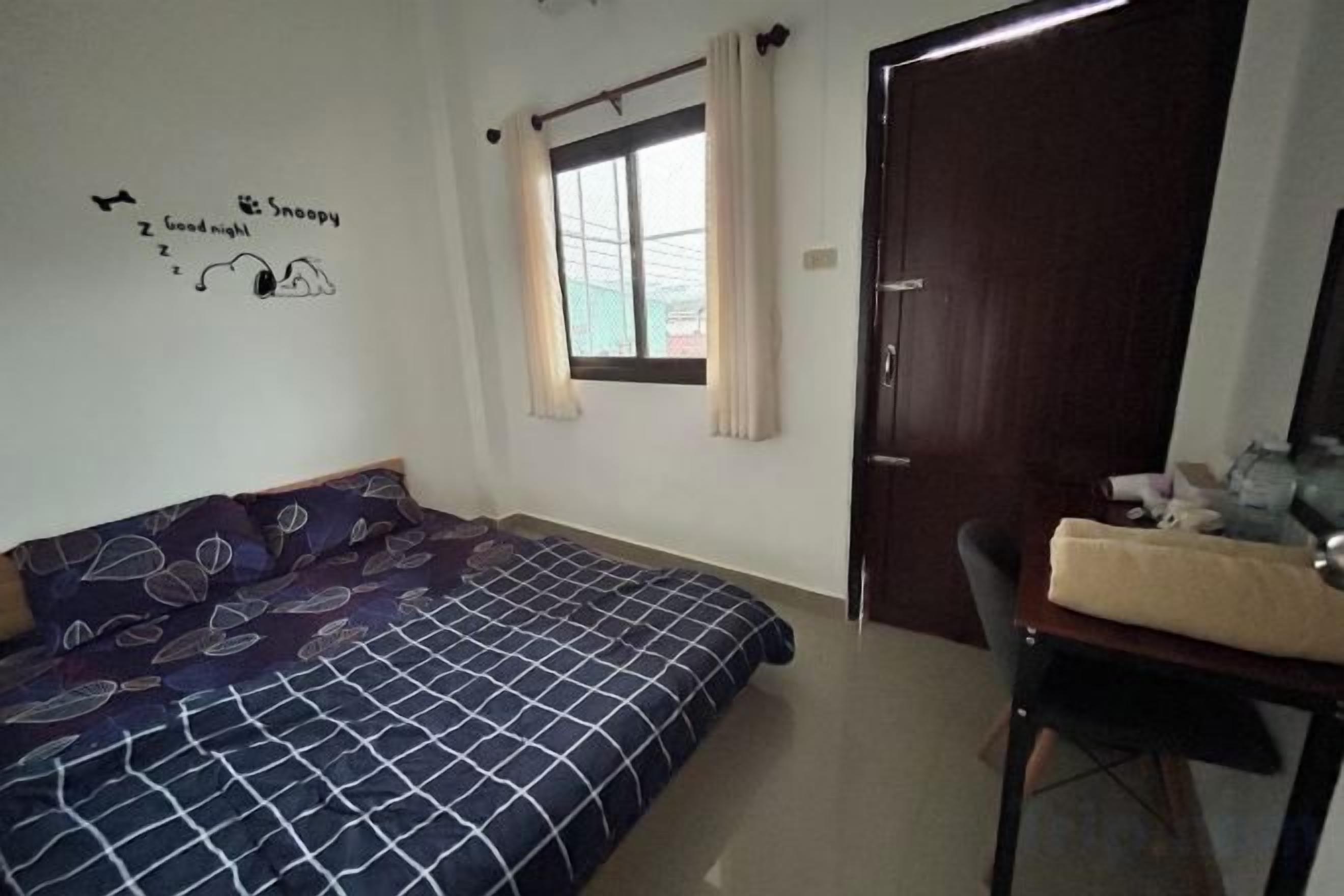 A bedroom with a bed, a desk, a chair, a window with curtains, and a door.