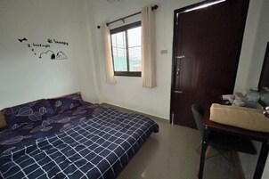 Un dormitorio con cama, escritorio, silla, ventana con cortinas y puerta.