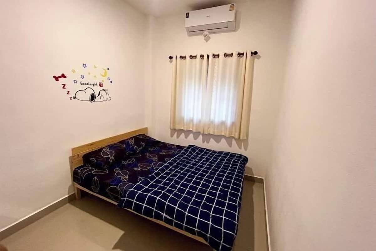 Un dormitorio pequeño con una cama individual, aire acondicionado de pared y una ventana con cortinas.