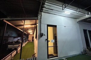 Un edificio con un espacio exterior techado, una puerta que da a una habitación y un estacionamiento cercado.