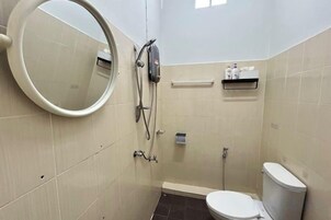 Un baño pequeño con inodoro, ducha, espejo y repisas con artículos de aseo.