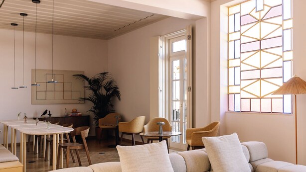 En moderne stue med sofa, stole, spisebord og et stort vindue med geometriske mønstre.