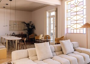 A modern living room with a sofa, chairs, a dining table, and a large window with geometric patterns. - Casamarela Health & Spa (Beja)
