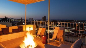 Tagterrasse med bålsted, siddepladser og udsigt over bybilledet i skumringen.