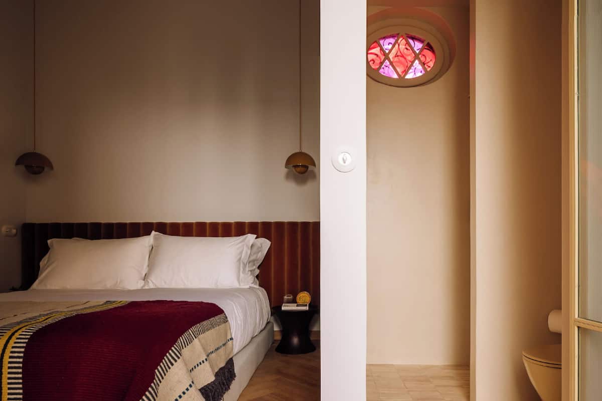 Ein Schlafzimmer mit einem Bett, zwei Pendelleuchten, einem Nachttisch und einem kleinen Tisch mit einer Uhr.