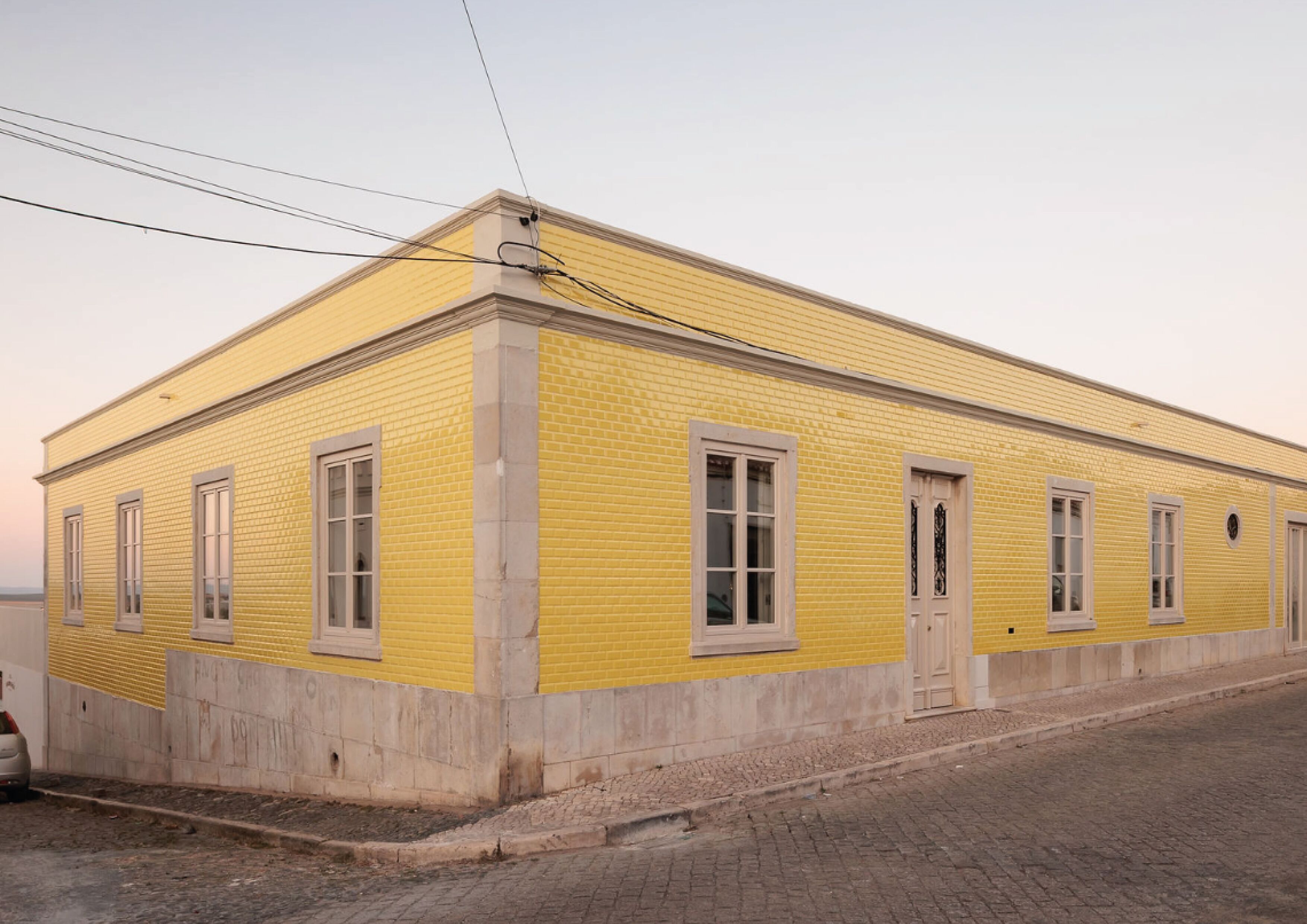 A yellow building with a flat roof, rectangular windows, and a door.