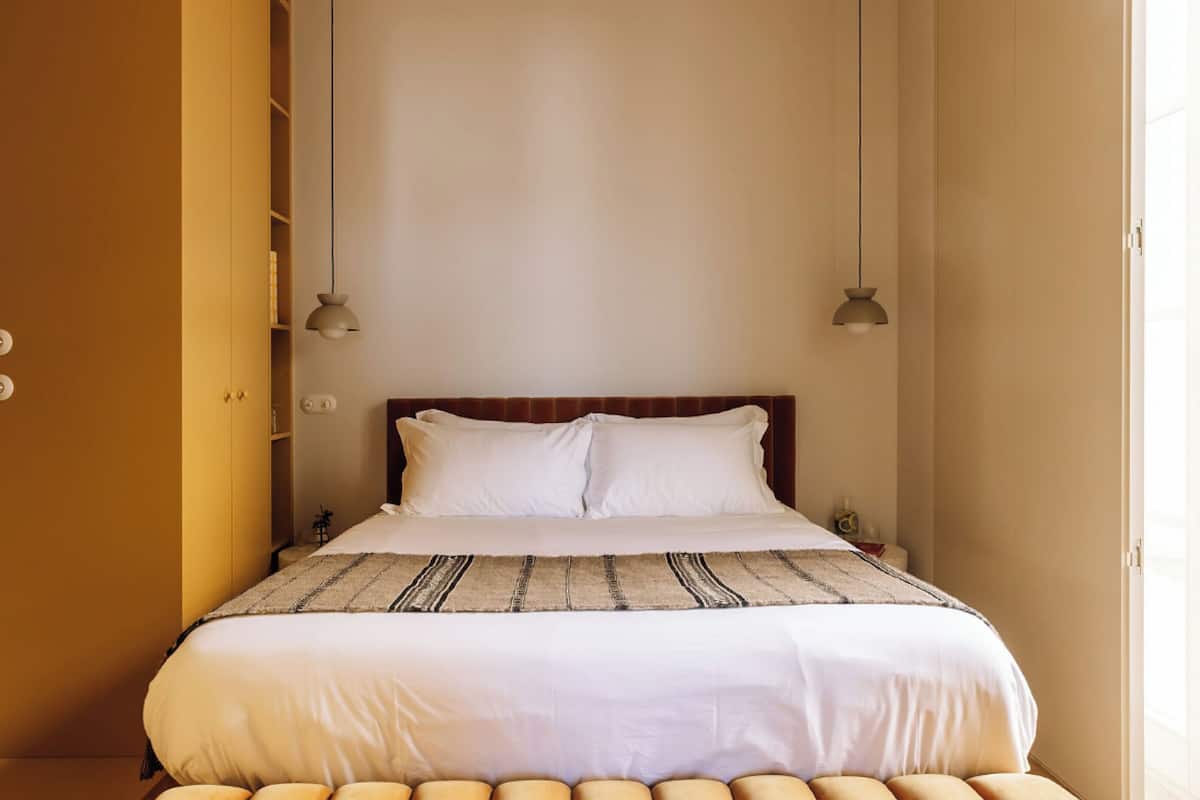 Ein ordentlich bezogenes Bett mit einer gestreiften Decke, einem hölzernen Kopfteil und zwei Pendelleuchten.
