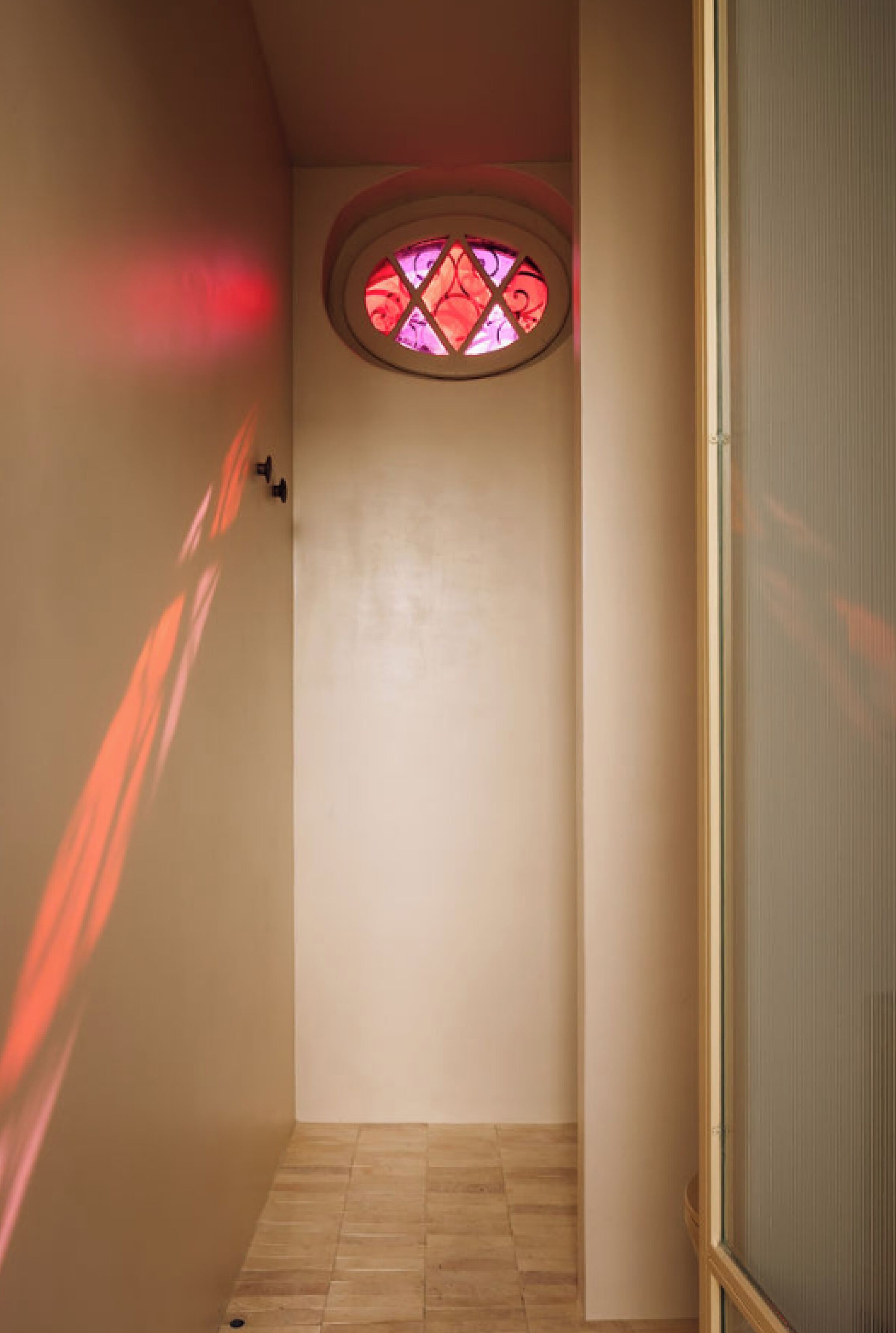 A narrow hallway with a stained glass window at the end, a door on the right, and a light fixture on the left.