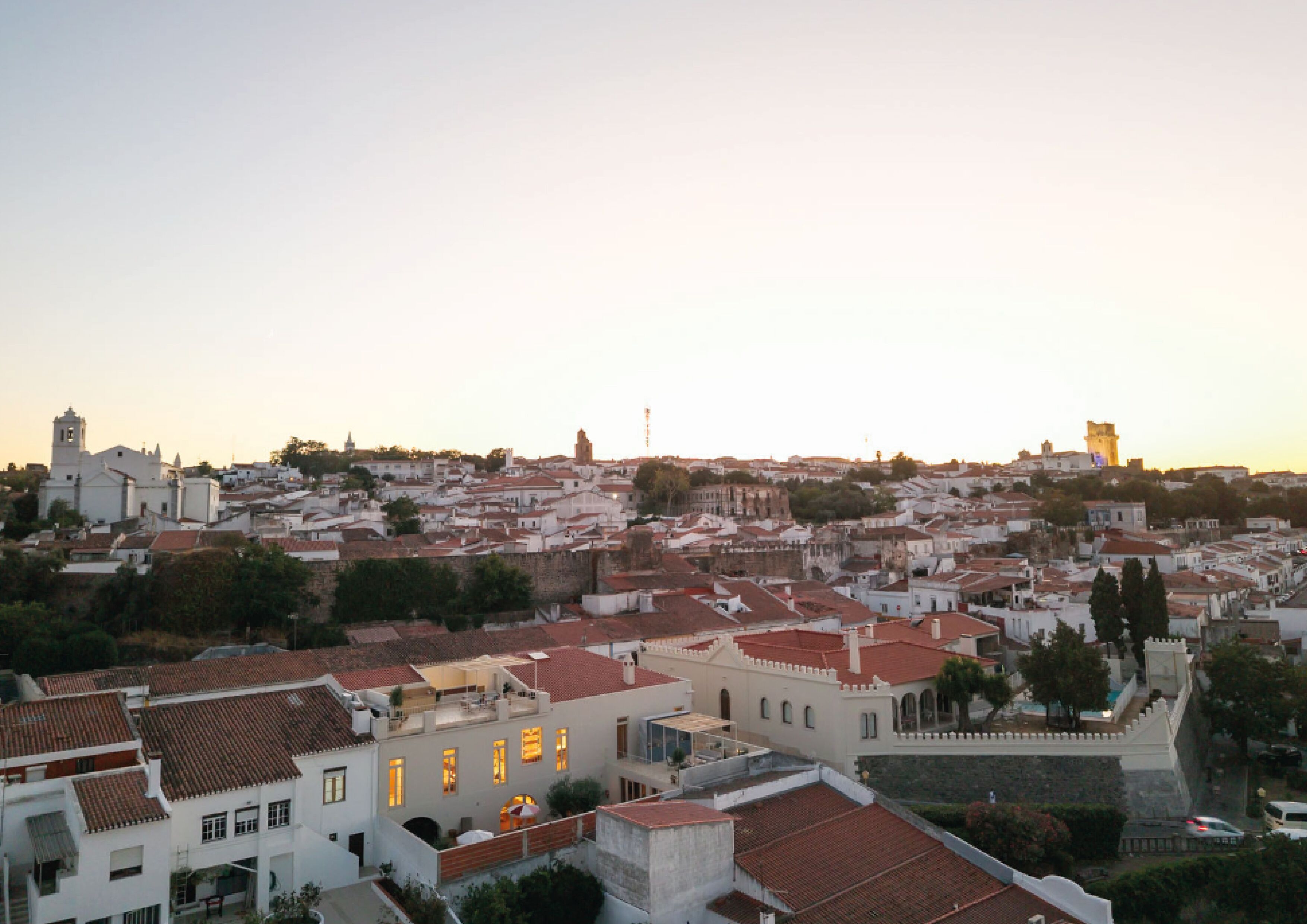 A historic town with white buildings and red-tiled roofs, featuring a prominent tower and a fortified wall.