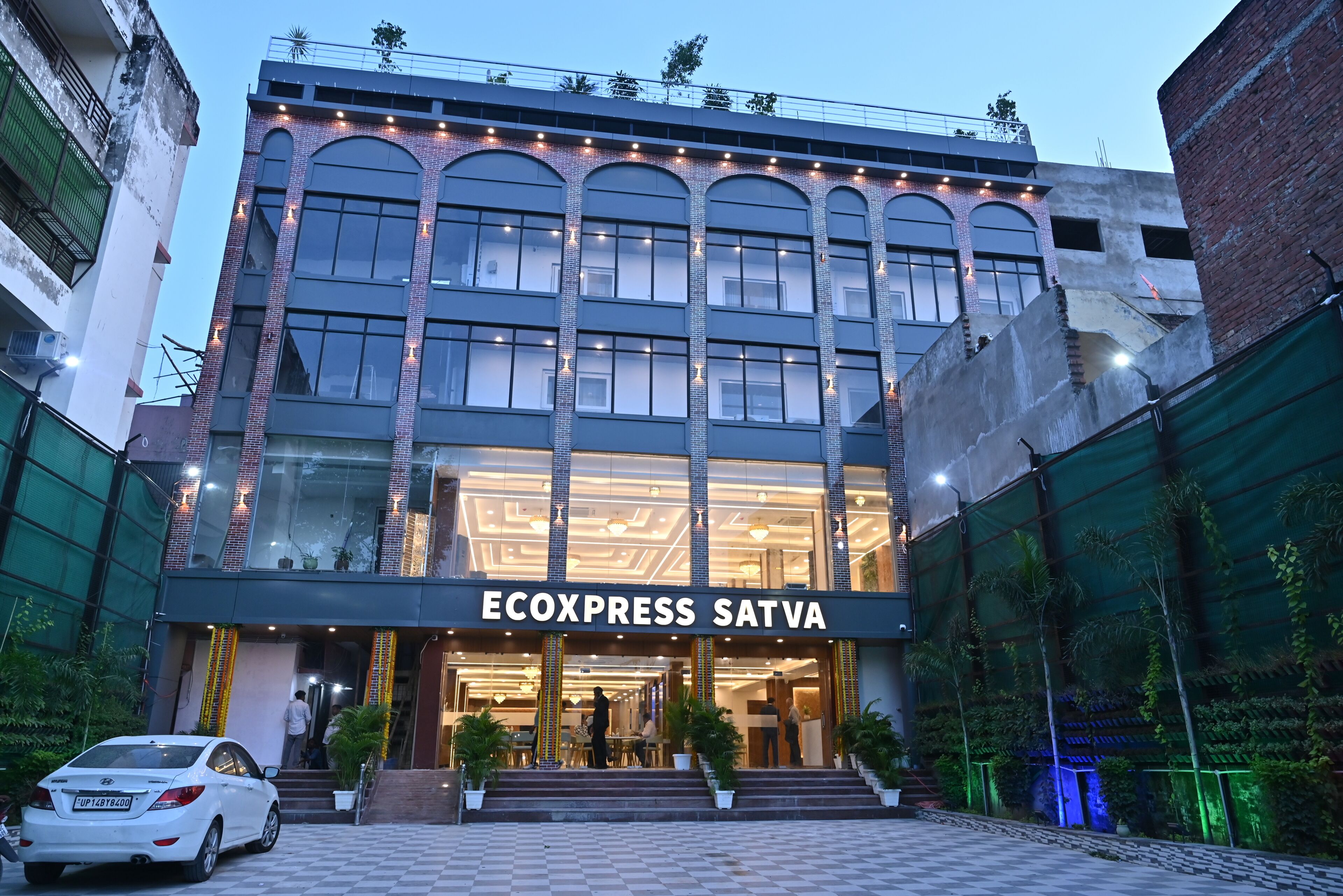 A hotel entrance with a name sign, a checkered pavement, and a white car parked in front.