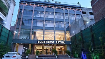 A hotel entrance with a name sign, a checkered pavement, and a white car parked in front.
