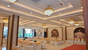 A banquet hall with round tables, white chairs, and chandeliers. - EcoXpress Satva Varanasi - Vegetarian with all Options (Varanasi)