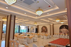 Un salón de banquetes con mesas redondas, sillas blancas y candelabros.