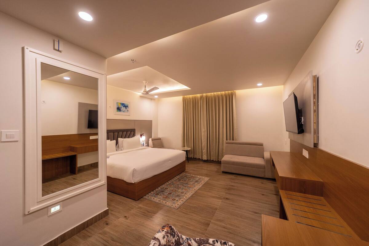 A modern hotel room with a large bed, a seating area, a flat-screen TV, and a ceiling fan.