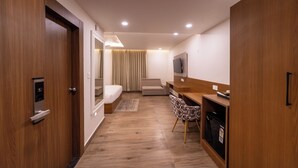 A modern hotel room with a wooden floor, a bed, a desk with a chair, a TV, and a wardrobe. - EcoXpress Satva Varanasi - Vegetarian with all Options (Varanasi)