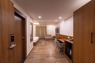 Une chambre d’hôtel moderne avec un plancher en bois, un lit, un bureau avec une chaise, une télévision et une armoire.