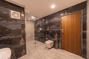 A modern bathroom with a glass-enclosed shower, a wooden door, and a marble wall with gold veins.