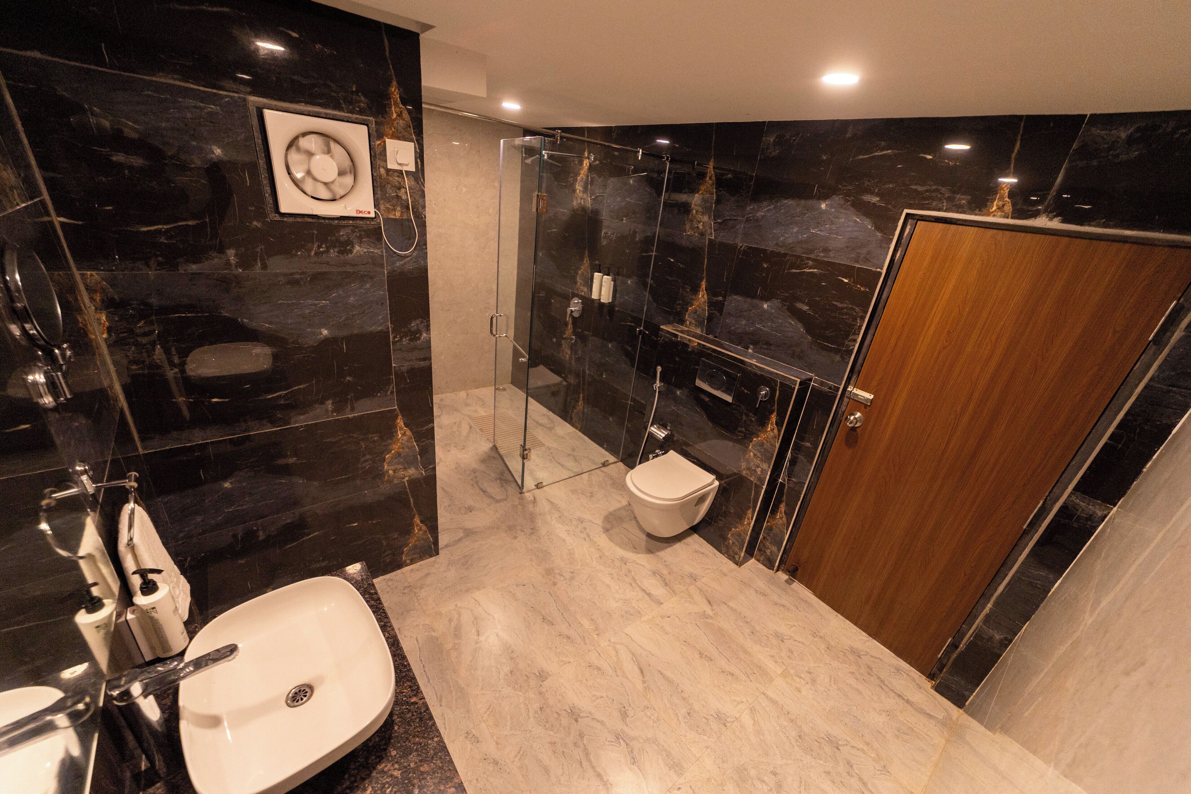 A modern bathroom with a marble floor, a white sink, a glass-enclosed shower, and a wooden door.
