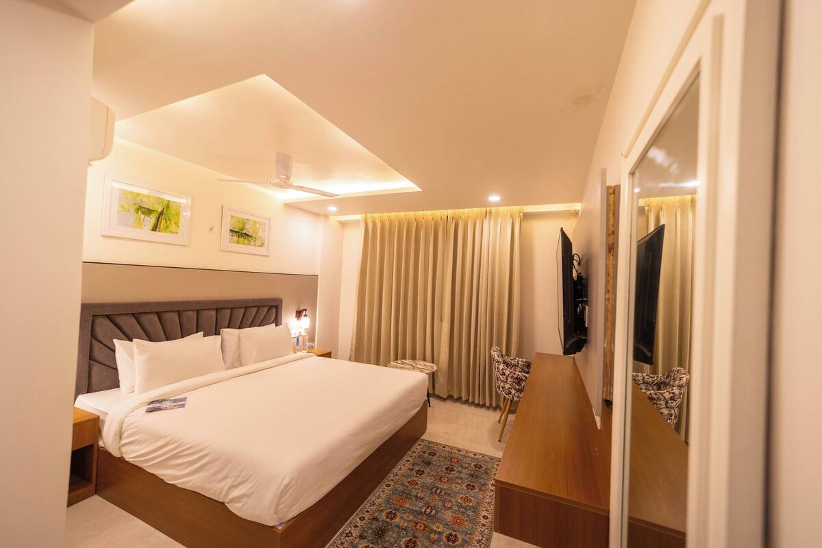 A hotel room with a large bed, a desk, a chair, a television, and a ceiling fan.
